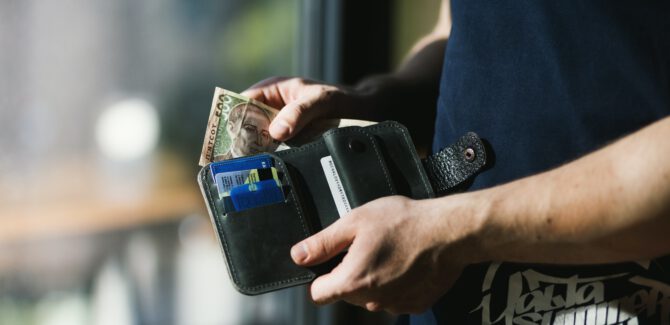 Mężczyzna wyciągający plik banknotów z portfela, które otrzymał jako zwrot prowizji z Santander Consumer Bank